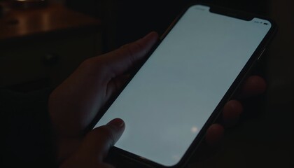 Close-up of a hand holding a phone with a blank screen, indicating unread messages in a dimly lit room
