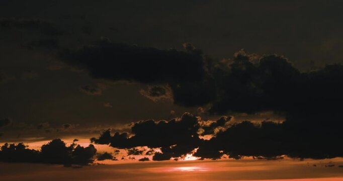 Timelapse close-up of orange and dark sunset sky with sun hidden behing moving contrasting black clouds
