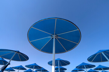 Blue parasols from below on the beach and pool under a clear blue sky with white painted poles at holiday location
