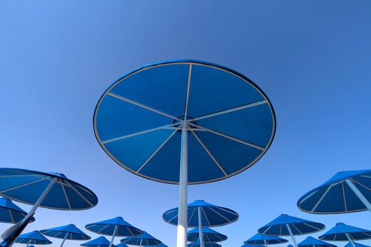 Blue parasols from below on the beach and pool under a clear blue sky with white painted poles at holiday location