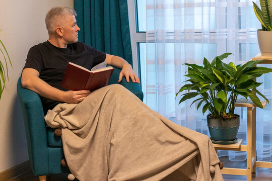 Man with the book sitting, reading in the cozy corner in the apartment on comfortable arm chair. People