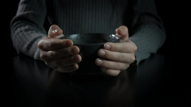 Empty bowl during economical crisis. A view of little hands hold a bold by the table and waiting for help during world crisis.