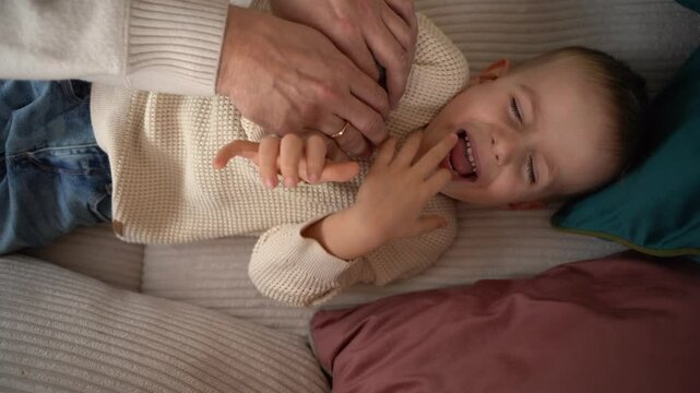 a dad tickles his 4-year-old son lying on the couch. High quality 4k footage