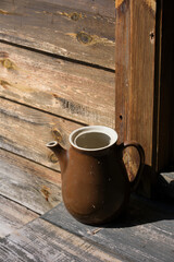 Ceramic milk or water jug placed in front of a wooden country house