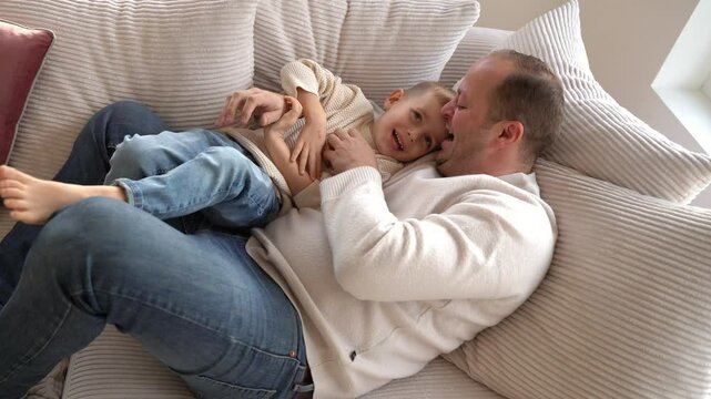 a dad tickles his 4-year-old son lying on the couch. High quality 4k footage