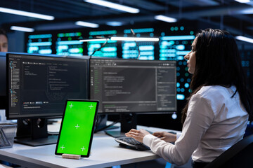 Computer scientists in data center checking equipment performance on green screen tablet after...