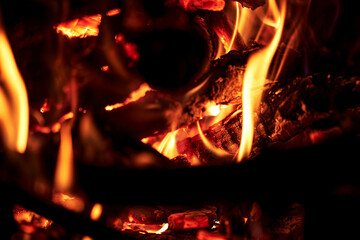 Burning firewood close-up bright flames orange and yellow colors intense heat glowing embers dark...