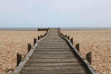 Obraz premium Weathered wooden board walk or path leading across shingle beach to the sea