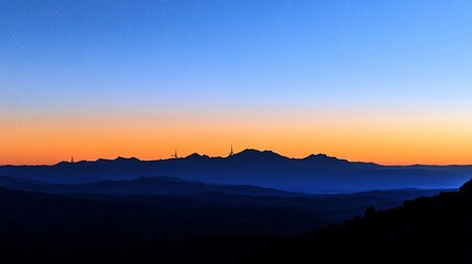 Fototapeta premium Silhouette of distant mountains at sunrise, vibrant orange and blue sky.