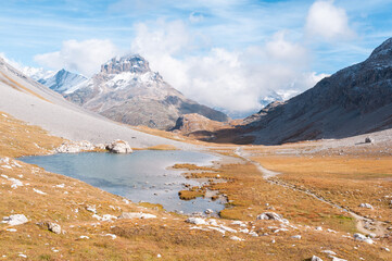 Clear blue mountain lake under clouds and a blue sky, with mountains in the background, called the Long Lake, in the Vanoise Massif, Savoie department, in the French Alps, France.