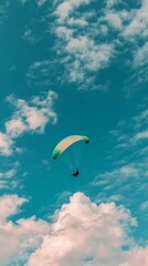 A single paraglider flies high above the clouds in a blue sky.