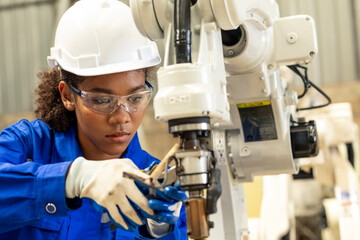 African american engineer woman fixing and testing an Artificial Intelligent welding robotic automatic arm machine in modern technology factory. Automation manufacturing for industry 4.0 Technology.