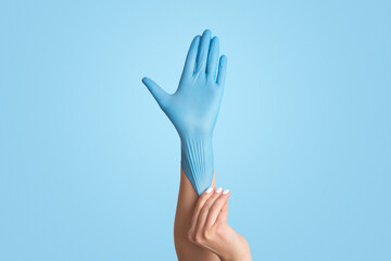 Infectious disease protection concept. Young female putting on blue medical glove against white...