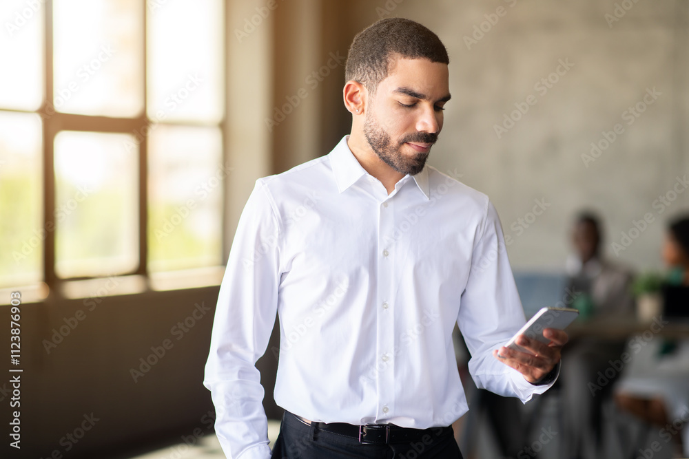 Poster a business professional checks his smartphone in a contemporary office environment. the warm lightin