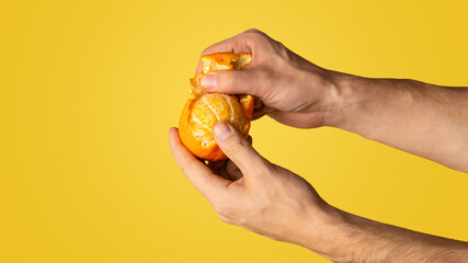 Fototapeta premium Millennial man peeling juicy orange on color background, closeup with copy space. Panorama