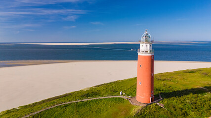 A unique perspective drone view at the lighthouse of Texel standing tall on a sandy beach, against a backdrop of the ocean waves crashing. The iconic red lighthouse of Texel Netherlands © Fokke Baarssen