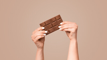 Unrecognizable millennial girl holding bar of chocolate on pink background, copy space. Panorama
