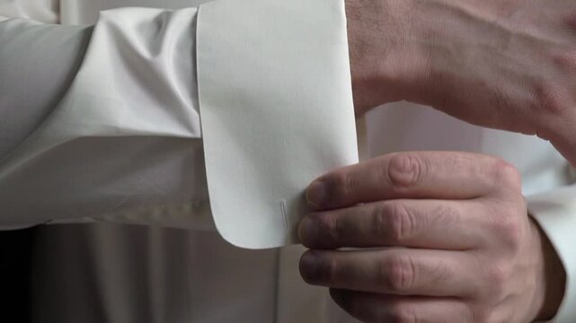 A detailed closeup of a hand skillfully fastening a cufflink on a pristine white formal shirt, showcasing elegance