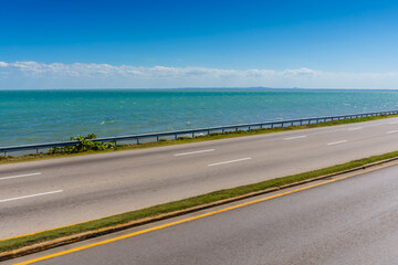 A long road with a grassy median and a blue ocean in the background