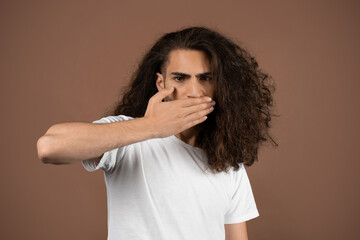 A guy with curly, long hair touches his face thoughtfully against a solid background. He embodies a...