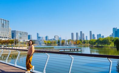 One Asian woman enjoying beautiful landscape of golden autumn season at Yinzhou Park, with lighthouse and urban CBD skyline in Ningbo, Zhejiang, China