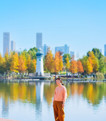 Fototapeta premium One Asian woman enjoying beautiful landscape of golden autumn season at Yinzhou Park, with lighthouse and urban CBD skyline in Ningbo, Zhejiang, China