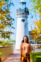 One Asian woman enjoying beautiful landscape of golden autumn season at Yinzhou Park, with white lighthouse and redwood trees in Ningbo, Zhejiang, China