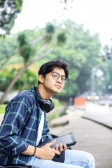 Casual Portrait of Young Student Man with Headphones Sitting on a Bench Park