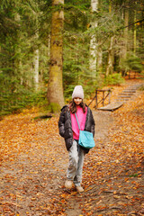 Fototapeta premium a teenage girl in a black jacket and hat on a path in an autumn forest.