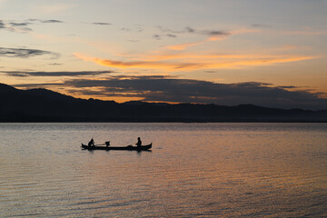 Silhouette of fisherman in the boat on the lake at sunset
