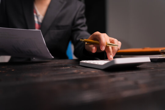 A young Asian man in a formal suit works late at night at his desk, analyzing stock market charts on a laptop and tablet, ensuring accuracy in financial data analysis.