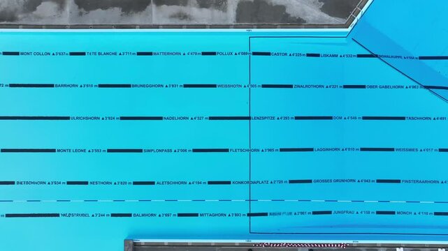 Close-up aerial top down pan across Swiss lap pool with clear lanes and names of mountains with elevation