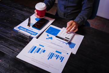 A man works late at night at his desk, hands close-up on charts and documents, conducting data...