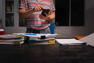 A man working late at home sits at his desk analyzing financial charts, checking stock market data on a laptop, tablet, and mobile, surrounded by informal, technology-driven tools.