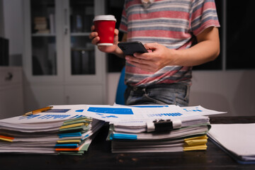 A man working late at home sits at his desk analyzing financial charts, checking stock market data on a laptop, tablet, and mobile, surrounded by informal, technology-driven tools.