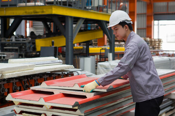 Young asian worker arranging lightweight wall roof sandwich panel for building material in a factory. He wear a hardhat and gloves for safety.