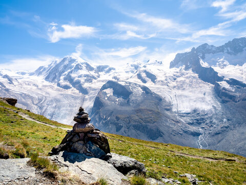 Cairn of rocks, stacked rock Zen pagoda on green grass hill on scenery of snow mountain view and blue sky background in the Swiss Alps at Zermatt, Switzerland on summer.