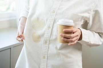 Cloth stain, disappointment asian young woman clumsy with hot coffee, tea stains on shirt, hand show making spill drop on white shirt, spot dirty or smudge on clothes at home, isolated on background