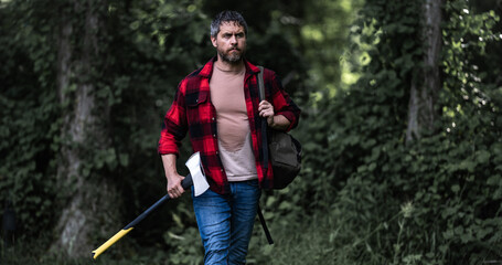 Hard working man with axe in forest. A bearded lumberjack with a large ax. Portrait of a brutal bearded man in a plaid shirt holds an axe. Male beauty and masculinity.