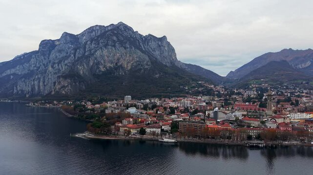 Lecco by lake como with mountain backdrop and calm waters on a cloudy day , aerial view