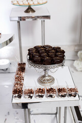 dessert table setting. In the foreground is a metal stand containing desserts covered in dark chocolate and decorated with gold sprinkles.