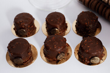 six small round cakes covered with chocolate icing with pieces of nuts. They are located on golden bases.