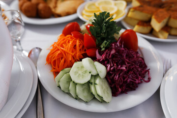 On the plate are slices of fresh cucumber, grated carrots, chopped red cabbage, halved cherry tomatoes and greens, possibly parsley. Other dishes are preserved in the background