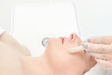 Fototapeta premium Caucasian female receiving skincare treatment in spa setting with dermabrasion tool for facial care.