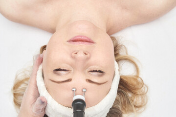 Female caucasian adult receiving facial microcurrent treatment in spa setting.