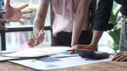 A group of people are gathered around a table with papers and a calculator. They are discussing and working on a project together