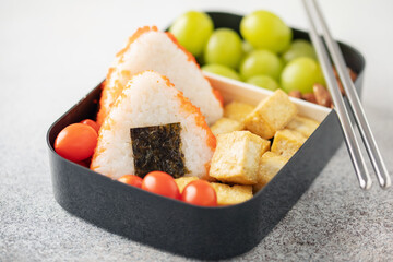 Vegan bento lunch with onigiri, tofu and fruits