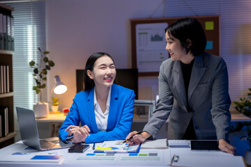 Two businesswomen working late and discussing about work in office at night