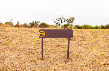 Wooden sign marks helicopter landing zone on mountaintop in middle of deep forest. Helicopter parking on brown grass field hills background. Helicopter parking sign for texture background bright sky.