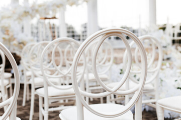 outdoor wedding ceremony. In the foreground are white chairs with round backs, arranged in several rows.